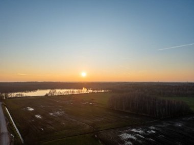 Sıcak renklerle süslenmiş, huzurlu bir manzarayı aydınlatan ve nazikçe akan bir nehri aydınlatan çarpıcı bir günbatımı manzarasına tanıklık etmek.