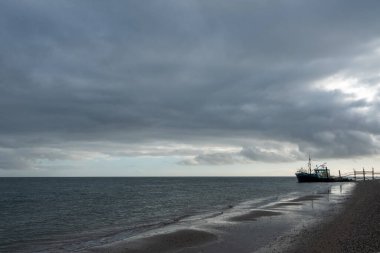 Eierland, De Cocksdorp, Texel, Hollanda, 28 Ekim 2024, Gri bulutlu gökyüzü altında küçük bir balıkçı teknesini gösteren nefes kesici ve dramatik bir deniz manzarası.