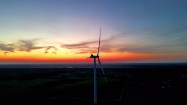 Nefes kesen bir günbatımı güzel siluetli bir rüzgâr türbini gökyüzünün canlı renklerine karşı diziliyor.