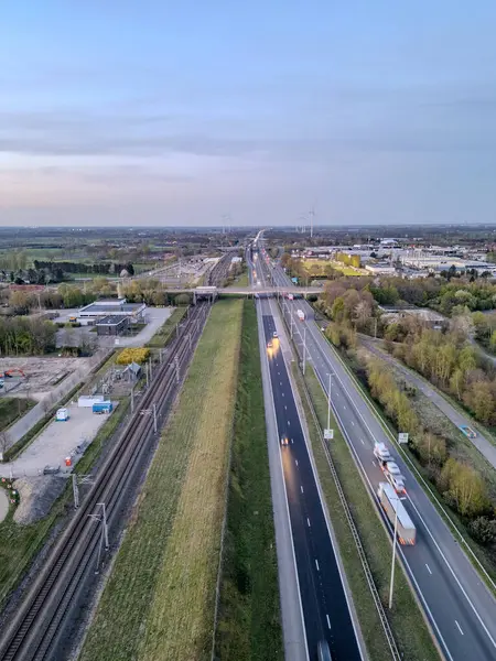 E19 Breda-Antwerp, Brecht, Antwerp, Belçika, 8 Nisan 2025 alacakaranlıkla tren yoluna paralel giden hareketli bir otoyolu çekiyor.