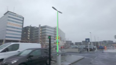 Schiphol Havaalanı, Amsterdam, Hollanda, 20 Aralık 2024, modern sokak lambaları ve yağmur bulutlarının yer aldığı şehir manzarası, canlı bir şehir atmosferini vurguluyor.