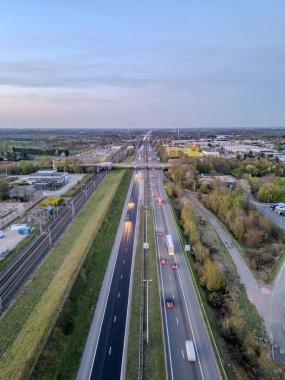 E19 Breda-Antwerp, Brecht, Antwerp, Belçika, 8 Nisan 2025, Yeşillik içinde yoğun bir otoyol görünüyor, arka planda geniş bir şehir manzarası var.
