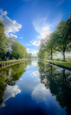 Huzurlu bir nehir manzarası canlı yansımalar, yemyeşil, ve başınızın üzerinde durgun mavi bir gökyüzü