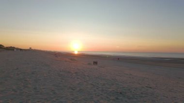 Huzurlu bir günbatımı güzel bir şekilde sahili aydınlatıyor, yumuşak dalgalar her yerde huzurlu bir ortam yaratıyor.