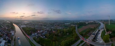 Lot, Beersel, Vlaams-Brabant, 22 Nisan 2025, gün batımında sakin doğa ve canlı şehir hayatı arasındaki uyumun büyüleyici bir görüntüsü.