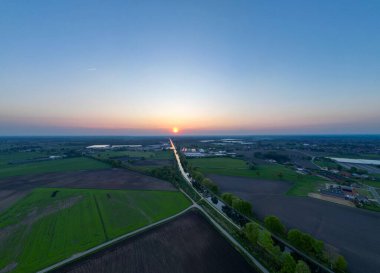 Çarpıcı bir günbatımı, sıcak renkleri tarlalara ve dolambaçlı bir yola serer, doğanın güzelliğini gözler önüne serer.