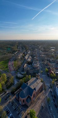 Brasschaat, Antwerp, Belçika, 8 Nisan 2025 'te havadan çekilen görüntü, tarihi bir kilise binasının yanındaki yemyeşil alanların yanında kentsel gelişimi güzel bir şekilde yakalıyor.