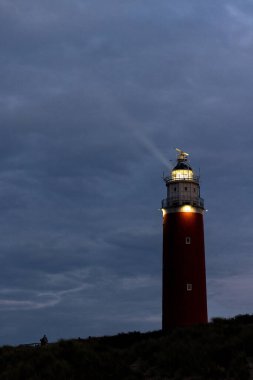 Eierland, De Cocksdorp, Texel, Hollanda, 28 Ekim 2024, Alacakaranlıkta karamsar ve dramatik bir gökyüzüne güçlü bir şekilde ışık saçan nefes kesici ve çarpıcı bir deniz feneri.
