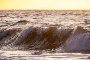 Okyanus dalgalarının nefes kesici güzelliğini tecrübe et. Uzaktaki ufukta çarpıcı bir altın gün batımı ile aydınlandı.