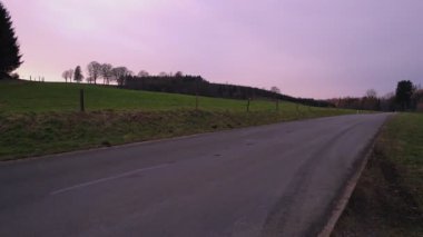 Huzurlu ve sakin kırsal bir yol, yemyeşil tarlalarla çevrili, büyüleyici alacakaranlık saatlerinde mükemmel bir şekilde yakalanmış.