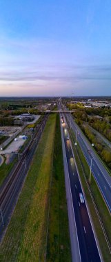 E19 Breda-Antwerp, Brecht, Antwerp, Belçika, 8 Nisan 2025, Aerial view güzel bir günbatımında yemyeşil ve ağaçlarla çevrili dolambaçlı bir otoyol gösteriyor.