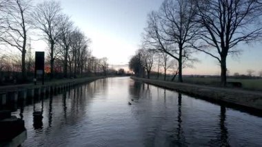 Sint Jozef, Rijkevorsel, Antwerp, Belçika, 27 Ocak 2025, sakin ve sakin bir kanal sahnesi sakin ve yansıtıcı sular, siluetli ağaçlar ve sakin bir akşam gökyüzü.