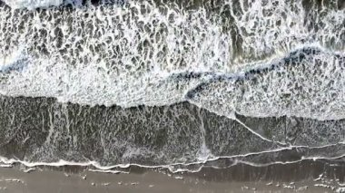 Çarpışan dalgaların hava görüntüsü büyüleyici kıyı şeridi boyunca karmaşık desenler ve dokular sergiliyor.