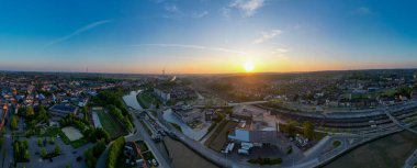 Halle, Vlaams Brabant, Belçika, 27 Nisan 2025, Sarmal bir nehir boyunca manzaralı kentsel bir alanı aydınlatan canlı bir günbatımını görüntüler.
