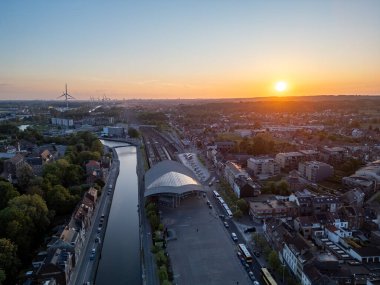 Halle, Vlaams Brabant, Belçika, 6 Mayıs 2025, canlı bir şehrin üzerinde nefes kesici bir günbatımı karmaşık mimarisini aydınlatır ve huzurlu su yollarını geliştirir.