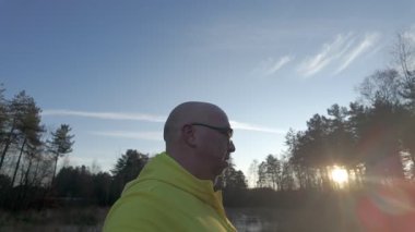 Huzurlu bir sahnede sarı kapüşonlu bir insan gün batımında doğada huzur içinde yürüyor.