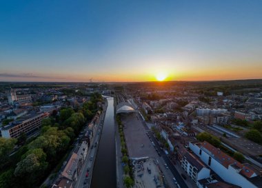 Halle, Vlaams Brabant, Belçika, 6 Mayıs 2025, serin bir nehir ve çevrenin canlı yeşilliğiyle nefes kesici bir şehir manzarası üzerine çarpıcı günbatımının tadını çıkarın.