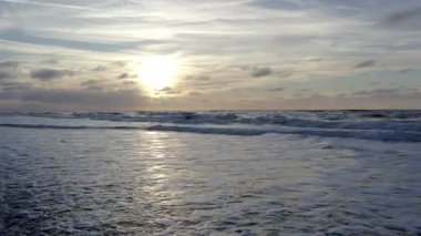 Güzel bir günbatımı okyanusun renklerini sarıyor. Yumuşak dalgalar kıyı boyunca süzülüyor ve sakin bir atmosfer yaratıyor.