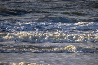 Sakin ve huzurlu bir okyanus manzarası alacakaranlıkta kumlu kıyıya hafifçe çarpıyor.