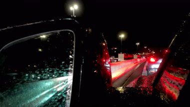 Büyüleyici bir gece sahnesi, araba camında yağmur damlalarıyla süslenmiş kaotik bir trafik sıkışıklığını resmediyor.