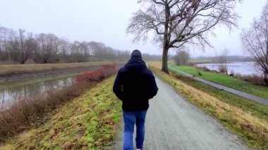 Huzurlu, sisli bir günde huzurlu bir nehir kenarında yürüyen yalnız bir figür derin bir sükuneti temsil eder.