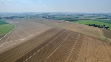 Bu hava manzarası arka planda canlı yeşillik parçalarıyla güzel sürülmüş tarım arazilerini sergiliyor.