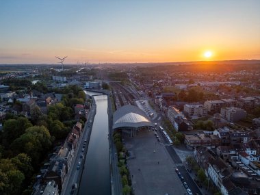 Halle, Vlaams Brabant, Belçika, 6 Mayıs 2025 çarpıcı günbatımında nehri ve modern mimarisi olan canlı bir şehir manzarası sergiliyor.