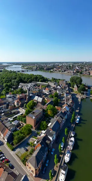 Klein-Willebroek, Willebroek, Antwerp, Belçika, 13 Mayıs 2025, çarpıcı bir hava manzarası yeşil ve demirli teknelerle çevrili dingin bir nehir kenti gösteriyor.