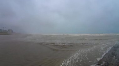 Bu sahne çalkantılı sular, kara bulutlar ve karamsar bir atmosferle dramatik bir sahil ortamı gösteriyor.