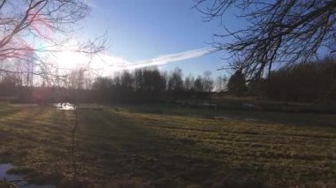 Güneş ışığı ağaçların arasından süzülürken sakin bir sahne, durgun suda yansımalar oluşturur.