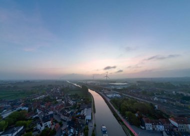 Lot, Beersel, Vlaams-Brabant, 22 Nisan 2025, huzurlu bir hava manzarası dingin bir alacakaranlık gökyüzünün altında yemyeşil bir nehrin ortasında güzel bir şekilde dönen bir nehri gösteriyor.