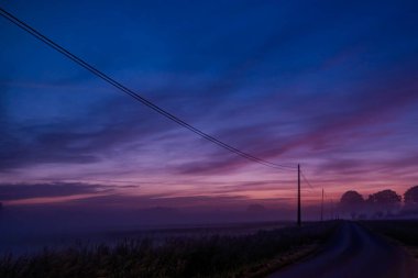 Canlı bir gökyüzü, dolambaçlı bir yol ve yumuşak alacakaranlık renklerinde uzak ağaçlarla huzurlu bir alacakaranlık manzarası.