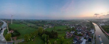 Lot, Beersel, Vlaams-Brabant, 22 Nisan 2025, sersemletici hava manzarası yemyeşil tarlaları ve gün doğumunda dolambaçlı nehir manzarası sergiliyor..