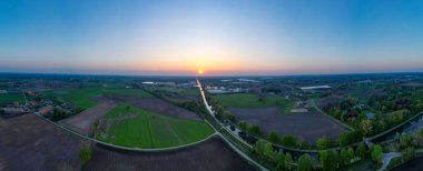 Rijkevorsel, Antwerp, Belçika, 27 Nisan 2025, engin tarlaları ve dolambaçlı yolları aydınlatan gün batımının nefes kesici ve çarpıcı görüntüsü.