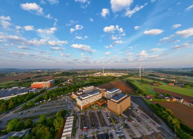 Colruyt, Wilgenveld, Halle, Vlaams Brabant, Belçika, 13 Mayıs 2025, çarpıcı bir hava perspektifi, yemyeşil alanlara ve geniş açık gökyüzüne karşı çeşitli kentsel binalar sergiliyor.