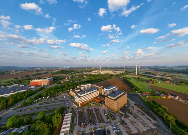 Colruyt, Wilgenveld, Halle, Vlaams Brabant, Belçika, 13 Mayıs 2025, çarpıcı bir hava perspektifi, yemyeşil alanlara ve geniş açık gökyüzüne karşı çeşitli kentsel binalar sergiliyor.