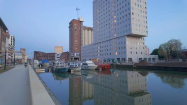 Kanaalkom, Leuven, Vlaams Brabant, Belçika, 23 Nisan 2025 günbatımında sakin sulara yansıyan teknelerin yanında modern binaların sergilendiği sakin bir kanal sahnesi.