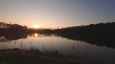 Nefes kesen bir gün batımı muhteşem ağaçlarla çevrili sakin ve sakin bir göle güzel bir şekilde yansıyor.