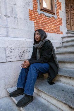 Bu görüntü, şehir binasının taş basamaklarında oturan genç bir Afro-Amerikalı kadını gösteriyor. Düşünceli ifadesi hareketli bir şehirde sessiz bir anı işaret ediyor. Modern çağının zıttı.