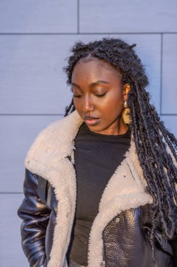 Görüntü, genç bir kadının derin düşüncelere daldığı, bakışlarının içe doğru eğildiği bir anı gösteriyor. Şık, siyah bir deri ceket giymişti. Pahalı, beyaz bir astarı vardı. Koyu rengiyle çelişiyordu.