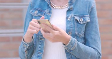 Bu yakın çekim modern iletişimin zarafetini, akıllı telefonunda ustalıkla gezinen bir kadın elinin detaylı bir görüntüsüyle yakalıyor. Şık kot giysisi ve şık aksesuar ipuçları.