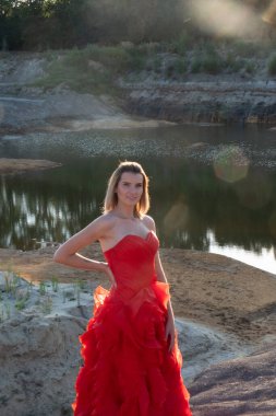 Nefes kesici ve çarpıcı bir model, zarif ve zarif bir şekilde, dingin bir su kütlesinin yanında canlı kırmızı bir elbiseyle poz verir.