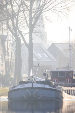 Rijkevorsel, Antwerp, 11 Mayıs 2024, sisli bir sabah, sakin kanalda, canlı ağaçlarla çevrili bir tekneyi gösteriyor.