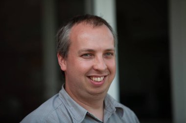 Neşeli bir adam sıcak bir şekilde gülümsüyor, güzel bir şekilde, pozitif ışıldayan parlak ve rahat bir ortamda yakalanıyor.