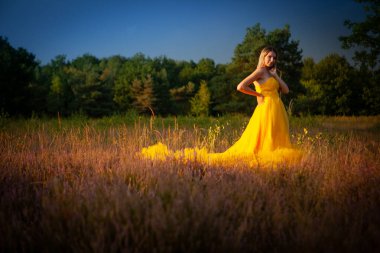 Şaşaalı ve zarif bir manken dalgalı sarı bir elbise giymiş sakin bir kır çiçeği tarlasının ortasında gururla duruyor.