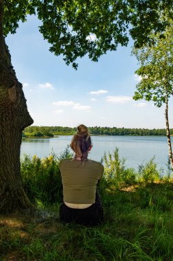 Huzurlu gölün kenarında sakin bir an, bir çocuk ve yetişkin arasındaki mutluluğu vurguluyor.