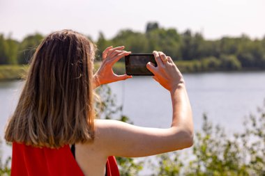 Serin bir nehir manzarasının güzelliğini yakalayan bir kadın, gelişen yeşillik arka planı mükemmel çerçeveliyor.