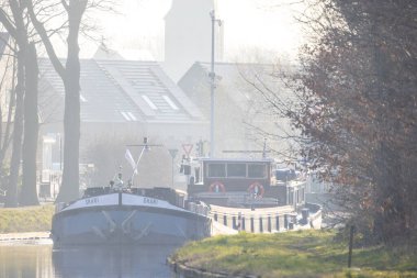 Rijkevorsel, Antwerp, 11 Mayıs 2024, Siste sakin bir manzara, bereketli ağaçlar ve güzel binalarla çevrili sakin bir kanalda gezinen tekneleri gösteriyor.