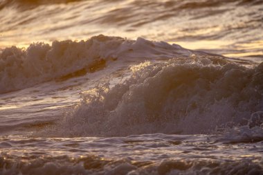 Okyanus dalgalarının büyüleyici görüntüsü altın bir günbatımının altında, doğanın dingin güzelliğini yakalıyor.