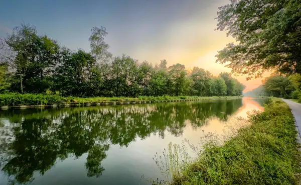 Huzurlu ve sakin bir nehir manzarası. Şafak vakti canlı yapraklar ve huzurlu su yansımaları sergiliyor.